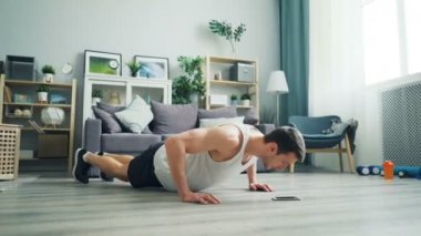 Güçlü fit genç adam yerde şınav yapıyor ve akıllı telefon ekranına bakıyor.