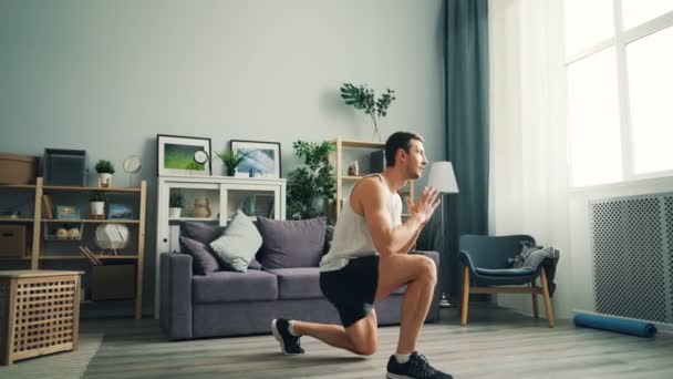 Guapo chico joven haciendo ejercicio en casa haciendo ejercicios deportivos para las piernas y el cuerpo . — Vídeos de Stock