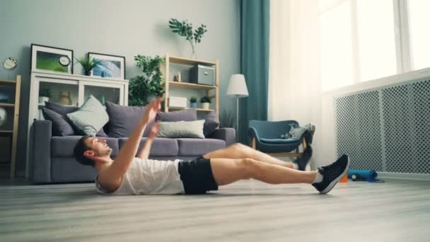 Cara ativo exercitando em casa fazendo esportes deitado no chão levantando pernas e braços — Vídeo de Stock