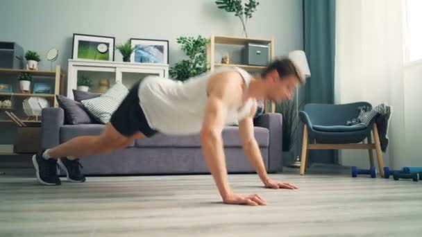 Joven hombre guapo aplaudiendo las manos mientras hace flexiones avanzadas en casa en el suelo — Vídeo de stock