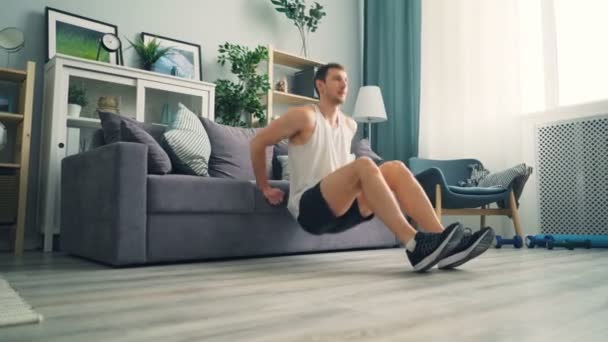Muscular guy doing push-up exercises working on arm muscles using sofa at home — Stock Video