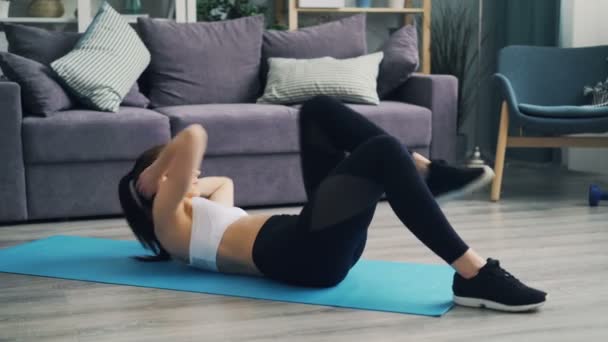 М'язиста молода леді, яка тренує м'язи живота на йога килимок вдома — стокове відео