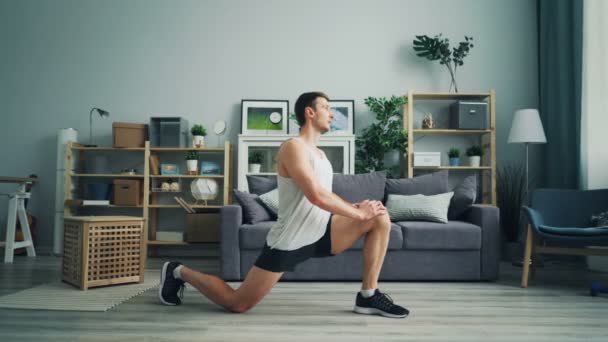 Bonito cara fazendo exercícios de alongamento em casa relaxando músculos tensos da perna — Vídeo de Stock