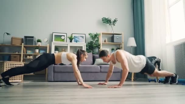 Joven hombre y mujer haciendo flexiones avanzadas y aplaudiendo juntas en piso — Vídeos de Stock