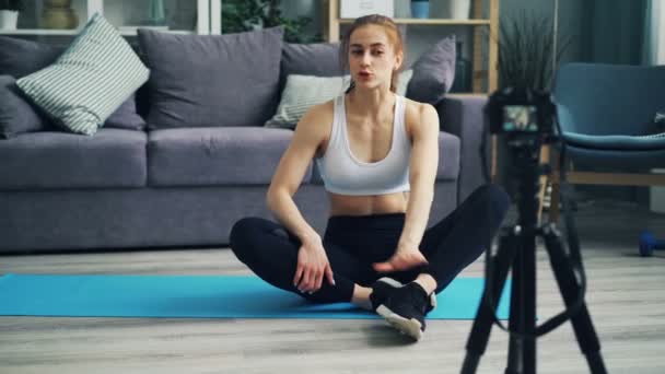 Jonge vrouw blogger opnemen van video praten en het doen van sport thuis op yoga mat — Stockvideo