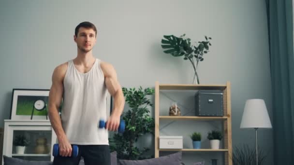 Chico guapo haciendo ejercicio con campanas mudas en casa levantando músculos de entrenamiento con pesas — Vídeos de Stock