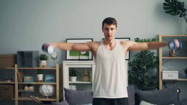 Красивый спортсмен, тренирующийся с гантелями, поднимающими оружие, практикующийся в доме — стоковое видео