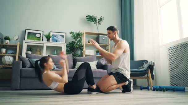 Jóvenes hombres y mujeres haciendo sentadas y aplaudiendo entrenamientos en casa — Vídeos de Stock