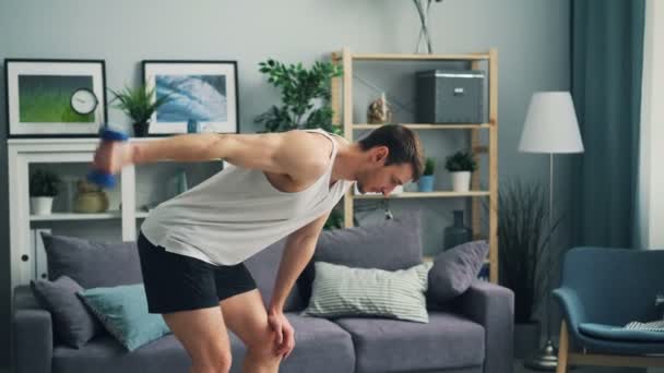 Joven haciendo ejercicios deportivos con mancuerna en casa levantando el brazo haciendo ejercicio — Vídeo de stock