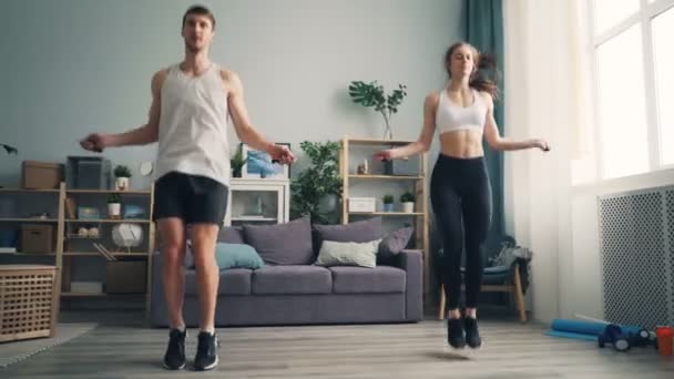 Молодой человек и женщина вместе прыгают через скакалку в доме и занимаются спортом в помещении — стоковое видео