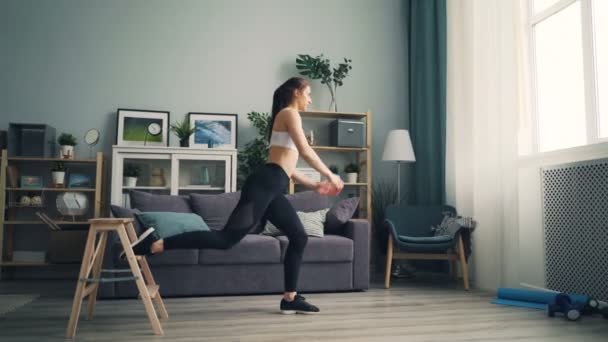 Aantrekkelijk meisje gehurkt op 1 been sport binnenshuis thuis doen met behulp van meubilair — Stockvideo