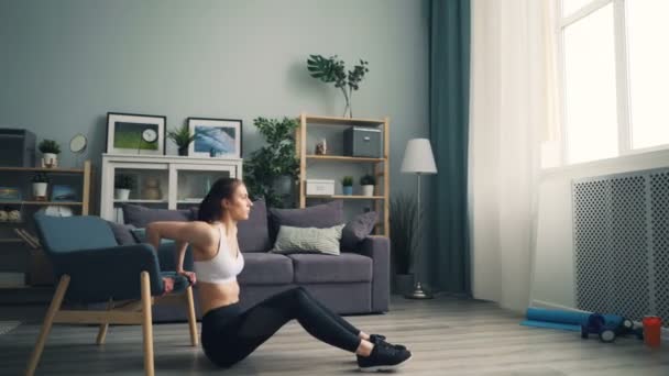 Csinos lány csinál pushup mártogatós otthon segítségével karosszék képzés apartman egyedül — Stock videók