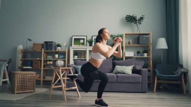 Мускулистая молодая женщина делает приседания в помещении, сконцентрированные на физических упражнениях — стоковое видео