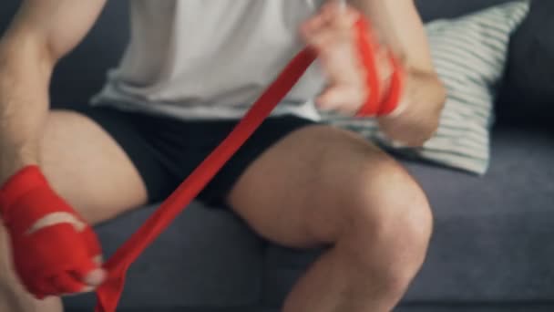 Чоловік-спортсмен обмотує руки обгортаннями зап'ястя перед тренуванням вдома — стокове відео