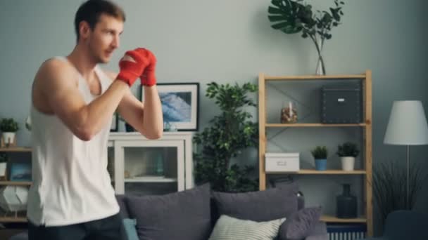 Muscular cara em sportswear boxe sozinho dentro de casa em apartamento desfrutando de atividade — Vídeo de Stock