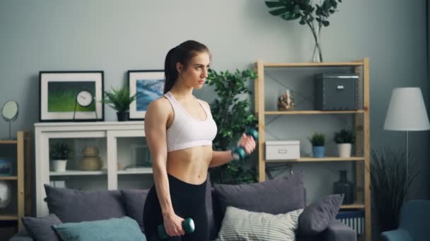 体重を持ち上げるに焦点を当てた自宅でダンベルと女性ボディービルダーのトレーニング — ストック動画