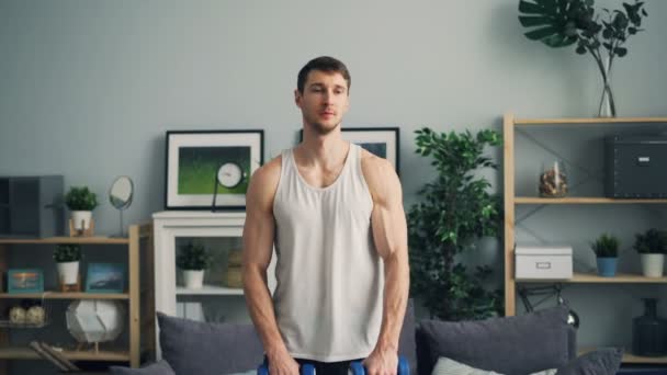 Musculoso chico entrenando con pesados tontos-campanas en apartamento levantando brazos respirando — Vídeos de Stock