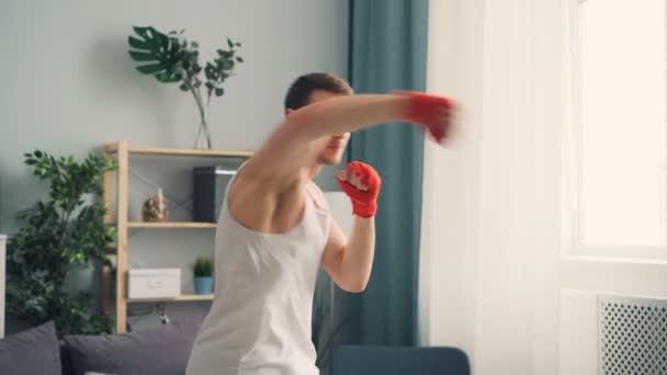 Guapo deportista con muñecas envueltas boxeando en el interior en casa haciendo ejercicio solo — Vídeos de Stock