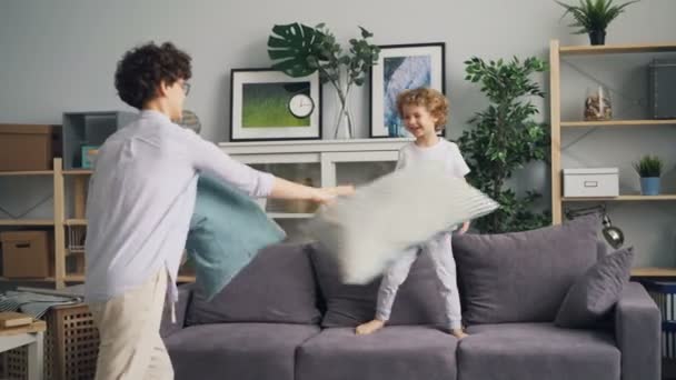 Giovane donna godendo lotta cuscino con piccolo bambino gettando cuscini sul divano — Video Stock