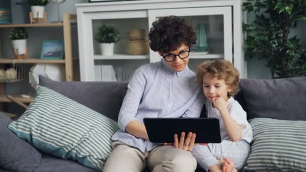 Мать и ребенок счастливая семья с помощью планшета трогательный экран и говорить дома — стоковое видео