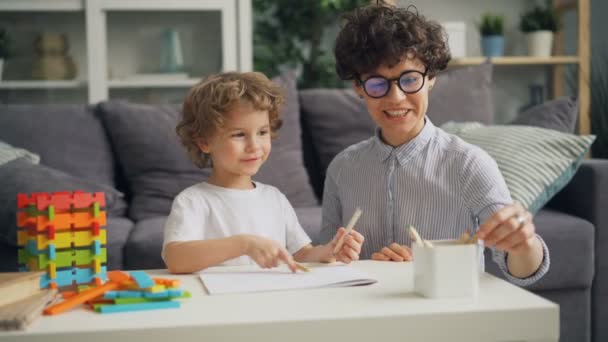 Pequeno menino desenho com lápis coloridos com mãe carinhosa no quarto aconchegante em casa — Vídeo de Stock