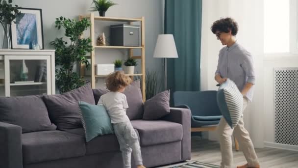 Feliz familia madre e hijo peleando almohadas en casa y riendo disfrutando del juego — Vídeos de Stock