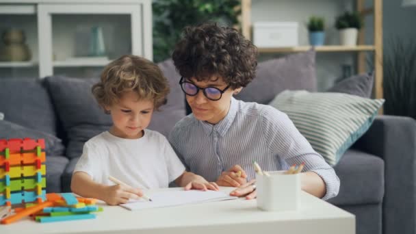 Sonriente niño está dibujando con lápices mientras madre cariñosa está hablando ayudando — Vídeos de Stock