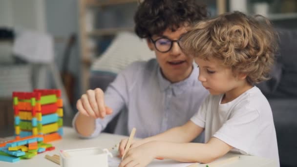 Αξιολάτρευτο παιδί σχεδιάζοντας εικόνα με μολύβια, ενώ η μητέρα μιλάμε και χαμογελαστός — Αρχείο Βίντεο