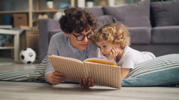 若い女性は彼女の息子の家の床に横になっている話を議論する本を読んで — ストック動画