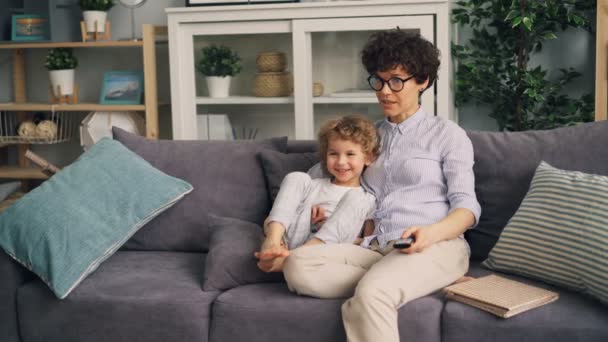 Mother and son watching TV at home talking and smiling sitting on sofa together — Stock Video