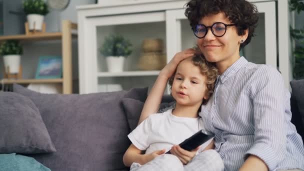 Joven mujer viendo la televisión con lindo chico acariciando y besándolo expresando amor — Vídeos de Stock