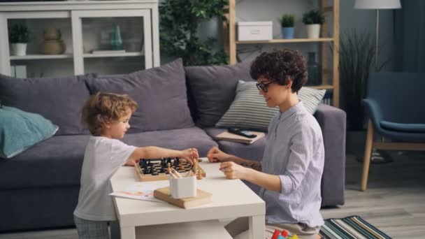 Jeune femme et heureux petit garçon jouant aux échecs à la maison puis faisant high-five — Video