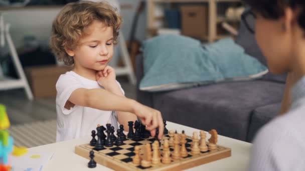 Smart kille spelar schack med mor rörliga delar uttrycker positiva känslor — Stockvideo