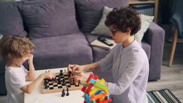 Мила дитина вчиться грати в шахи і розважатися з веселою молодою мамою — стокове відео