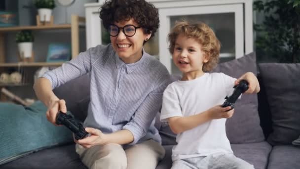 Маленький хлопчик грає у відеоігри з збудженою мамою, що тримає джойстики вдома — стокове відео