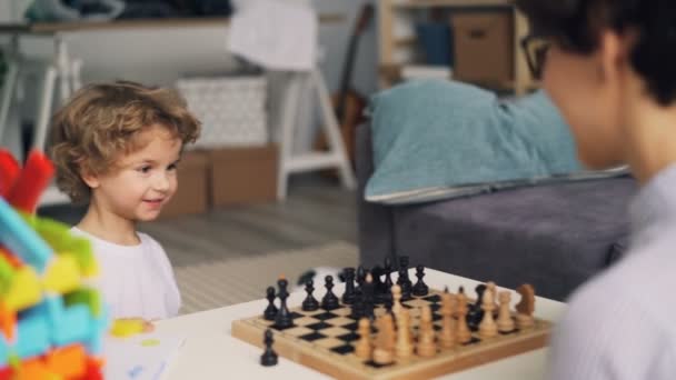 Madre enseñando a lindo niño a jugar al ajedrez mientras el niño se divierte moviendo piezas — Vídeo de stock