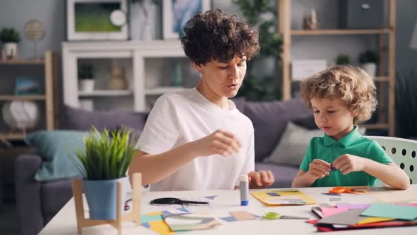 Niño y su mamá haciendo collage cortando figuras de papel pegadas con pegamento — Vídeos de Stock