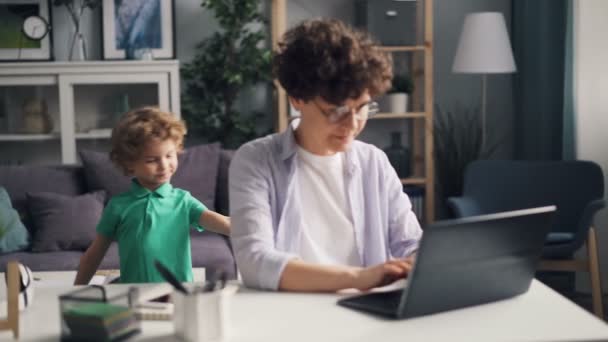 Θηλυκό ελεύθερος επαγγελματίας εργάζεται με φορητό υπολογιστή, στη συνέχεια, παίζοντας με το μικρό παιδί στο σπίτι — Αρχείο Βίντεο
