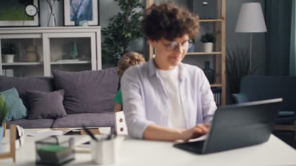 Meisje met laptop werkt dan in gesprek met haar zoon en zoenen hem spelen — Stockvideo