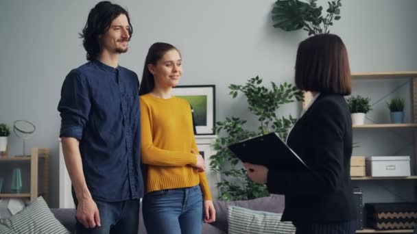 Leende mäklaren ger nyckeln till nya ägare och skakar händer, par kyssar — Stockvideo