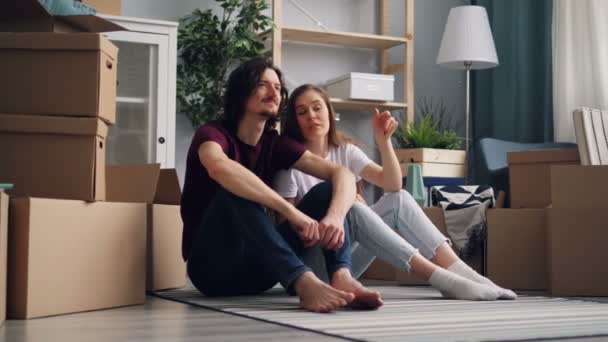 Девушка и парень пара говорят сидя на полу в новой квартире с коробками — стоковое видео