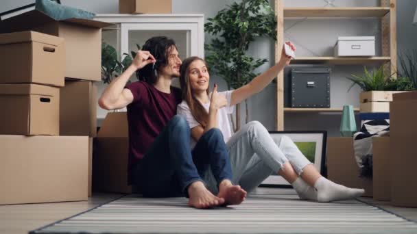 Chica y chico tomando selfie con llaves en casa nueva utilizando la cámara de teléfono inteligente moderno — Vídeos de Stock