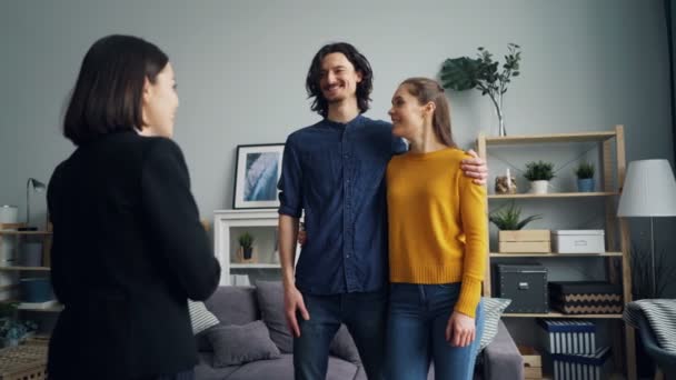 Realtor dando la clave a los nuevos propietarios estrechando la mano, feliz pareja besándose y abrazándose — Vídeos de Stock