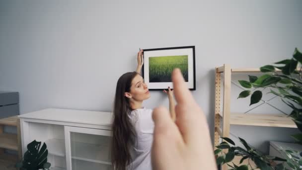 Menina bonita pendurado imagem na parede, enquanto o homem escolhendo lugar mostrando polegares para cima — Vídeo de Stock