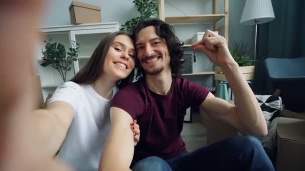 POV του χαριτωμένο ζευγάρι παίρνοντας selfie στο σπίτι με νέα κλειδιά του σπιτιού που δείχνει τους αντίχειρες-up — Αρχείο Βίντεο