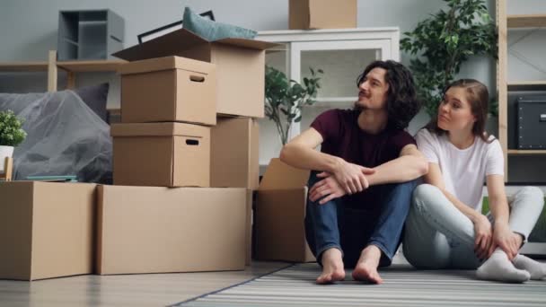 Mladá žena, která mluví s manželem a sedí na podlaze s krabic během přemístění — Stock video