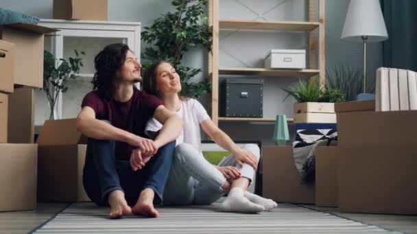 Gelukkig paar praten glimlachen bespreken nieuwe flat zittend op de vloer met dozen — Stockvideo