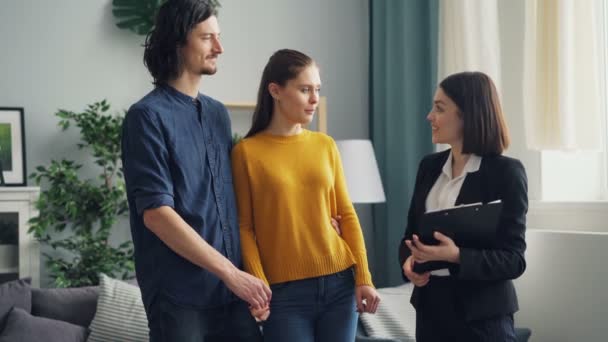 Homem e mulher conversando com agente imobiliário feminino e discutindo documentos dentro de casa — Vídeo de Stock