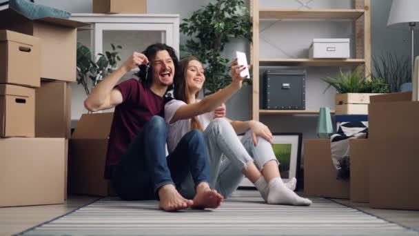 Pareja feliz tomando selfie con llaves usando la cámara del teléfono inteligente en nuevo apartamento — Vídeos de Stock