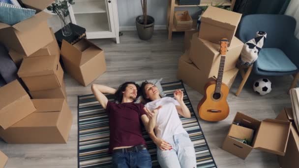 Man en vrouw praten over interieur liggend op de vloer in een nieuw huis rond dozen — Stockvideo